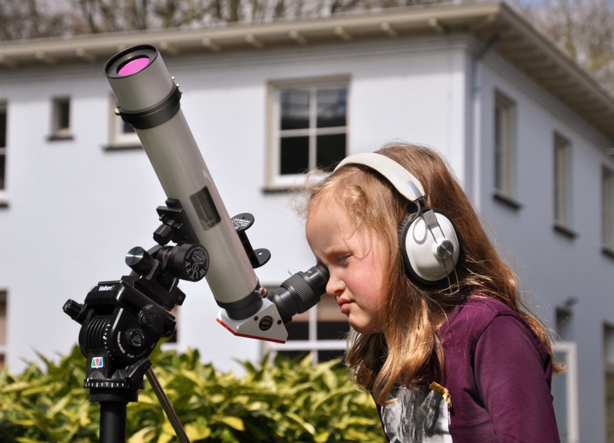 Een meisje kijkt door een telescoop naar de zon in de tuin van Sonnenborgh 